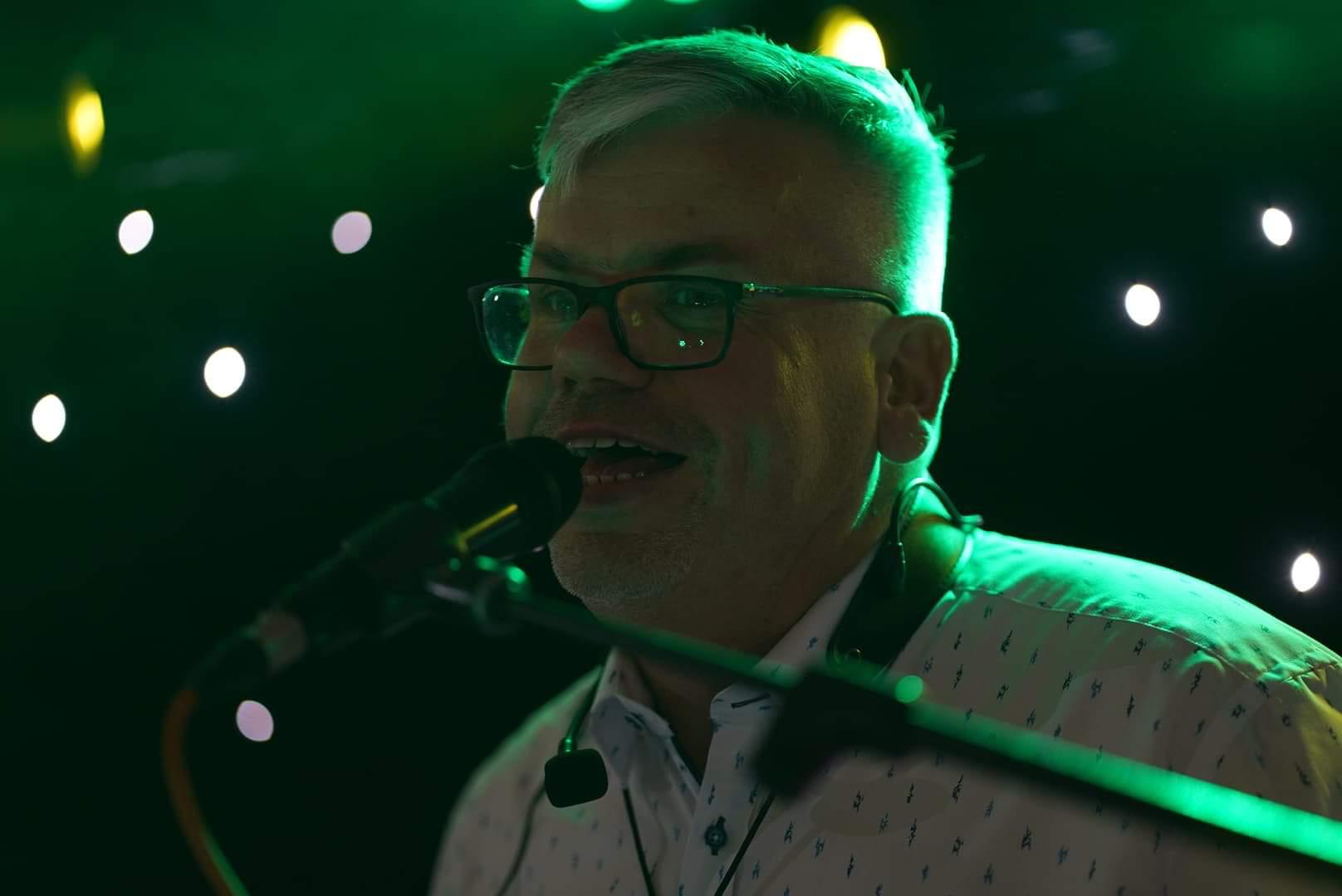 Wojtek śpiewa do mikrofonu na tle świateł scenicznych